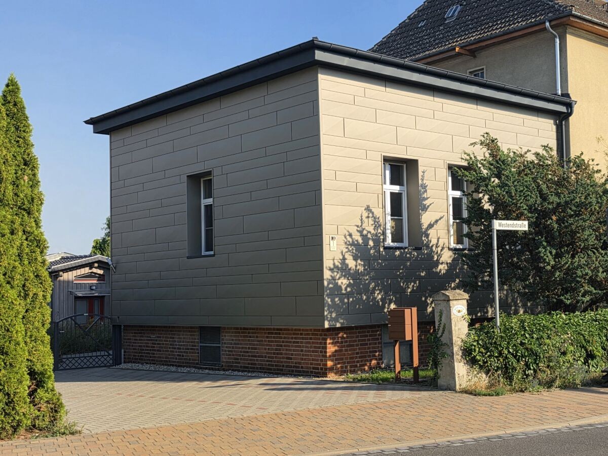 Straßenansicht des Zahna-Lofts mit moderner grauer Fassadenverkleidung und Klinkersockel