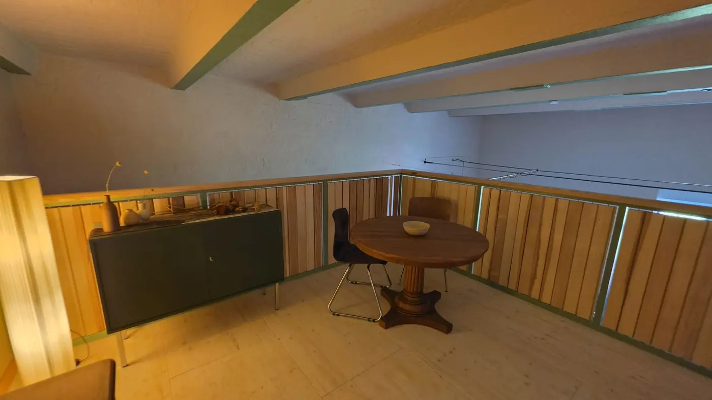 Sitzplatz auf der Galerieebene der Ferienwohnung Zahna-Loft — runder Tisch mit Stuhl vor Sideboard und Holzgeländer