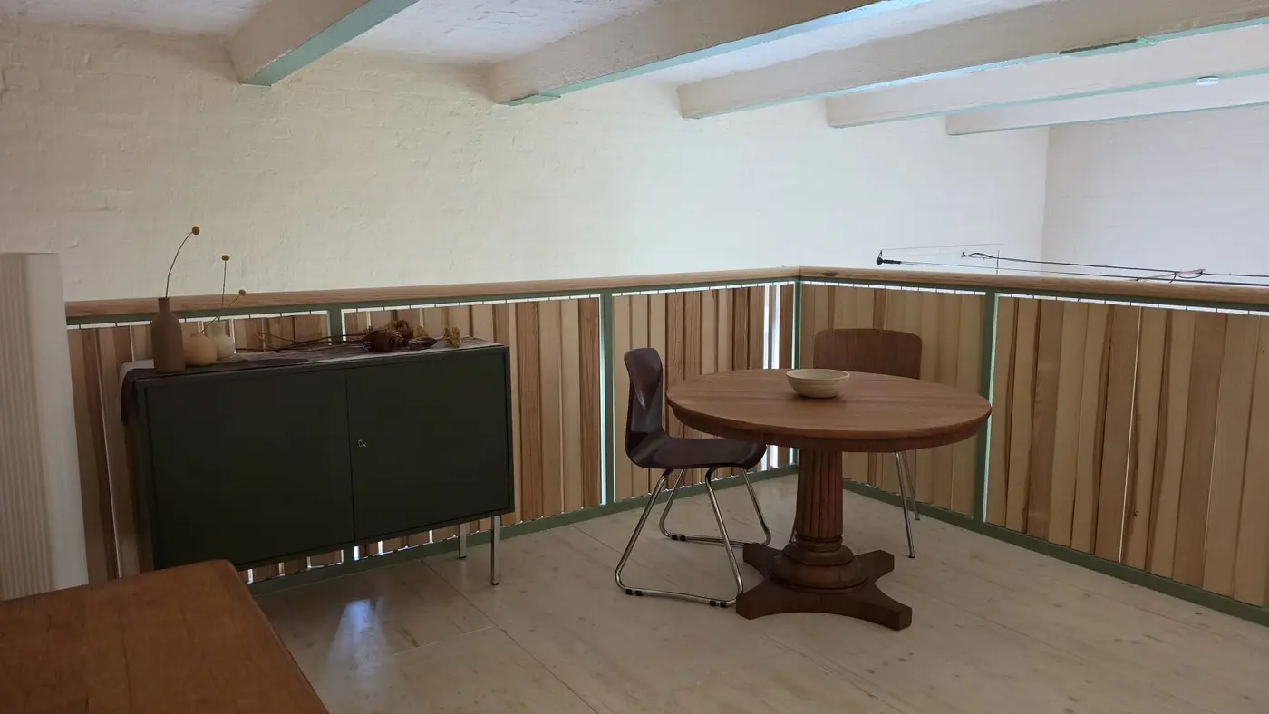 Sitzplatz auf der Galerieebene der Ferienwohnung Zahna-Loft — runder Tisch mit zwei Stühlen vor dem dekorierten grünen Sideboard und der weiß gekalkten Ziegelwand