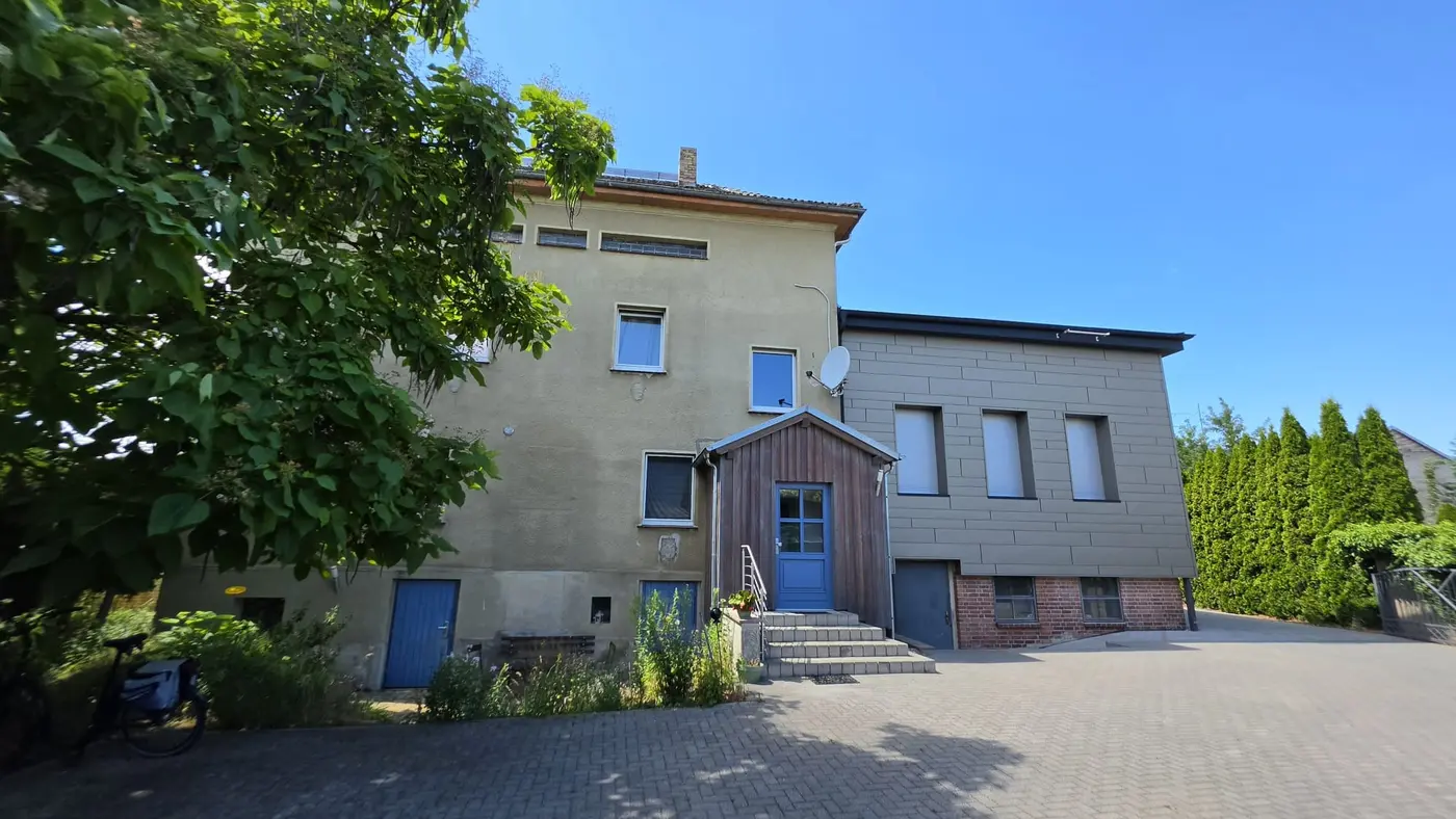 Außenansicht des Hauses der Ferienwohnung Zahna-Loft — Hof mit Bäumen, gepflasterter Einfahrt und blauen Türen