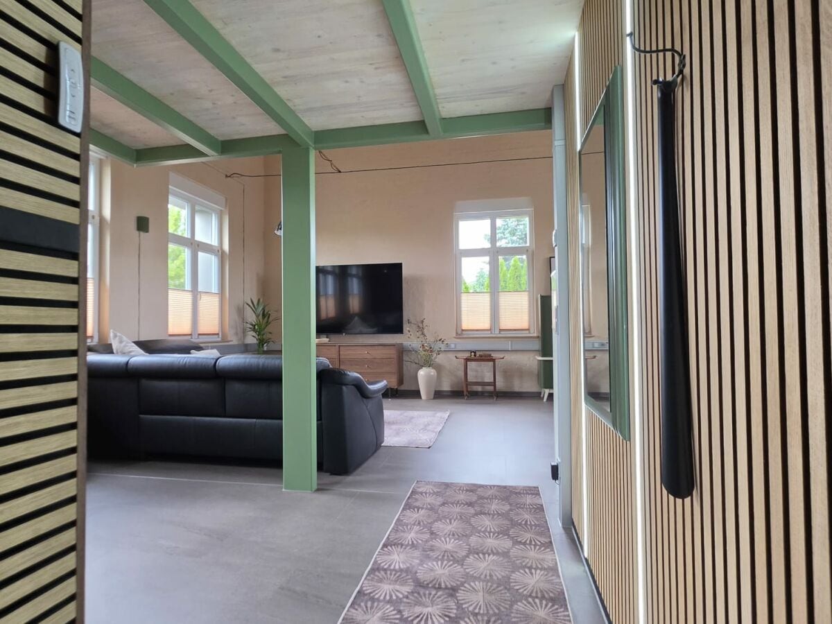 Blick vom Eingang in den offenen, loftartigen Wohn- und Essbereich mit grün lackierten Holzbalken und hohen Fenstern