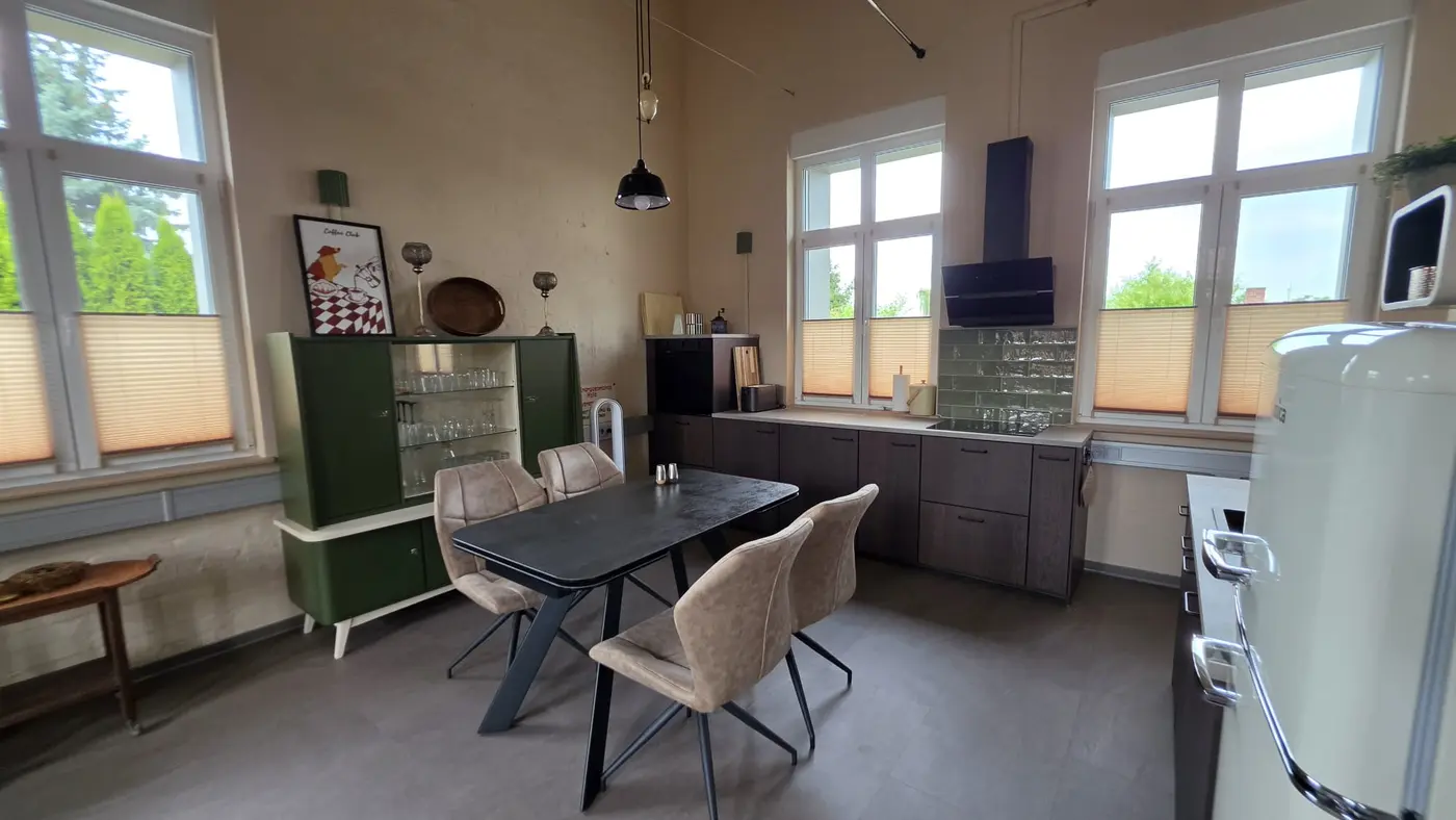 Offene Wohnküche mit Esstisch, hellen Polsterstühlen, grüner Vintage-Vitrine und dunkler Kochzeile