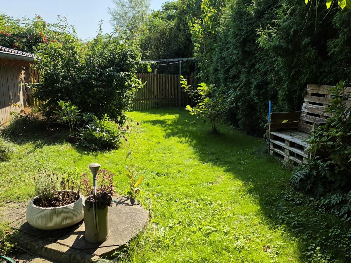 Eingezäunter Naturgarten mit Sitzbank aus Palettenholz, umgeben von Hecken und Sträuchern
