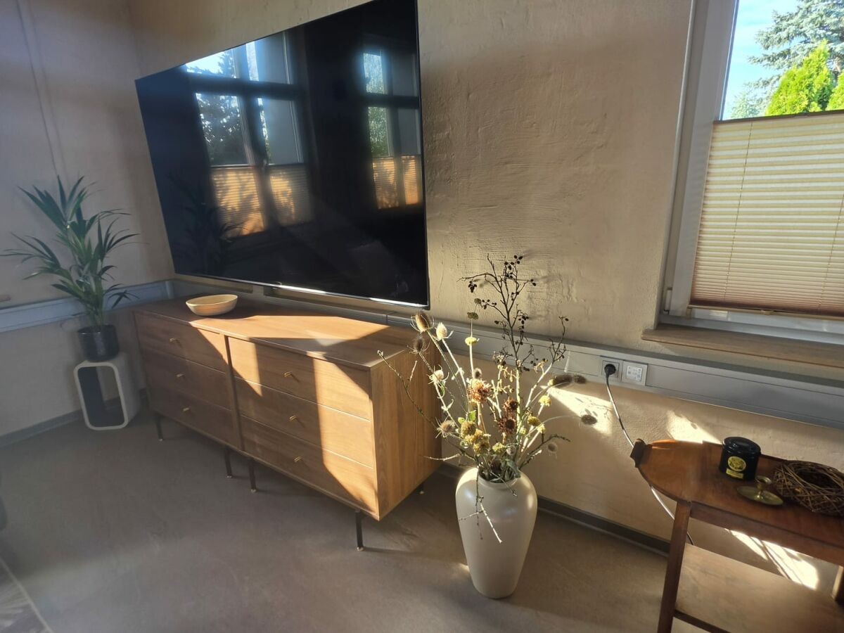 Wohnbereich mit Holz-Sideboard, Zimmerpflanze und großer Vase in warmem Abendlicht