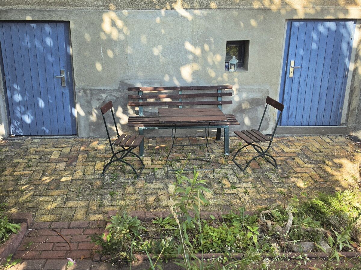 Sitzecke im Senkgarten mit Holzbank, Tisch und Stühlen zwischen zwei blauen Türen