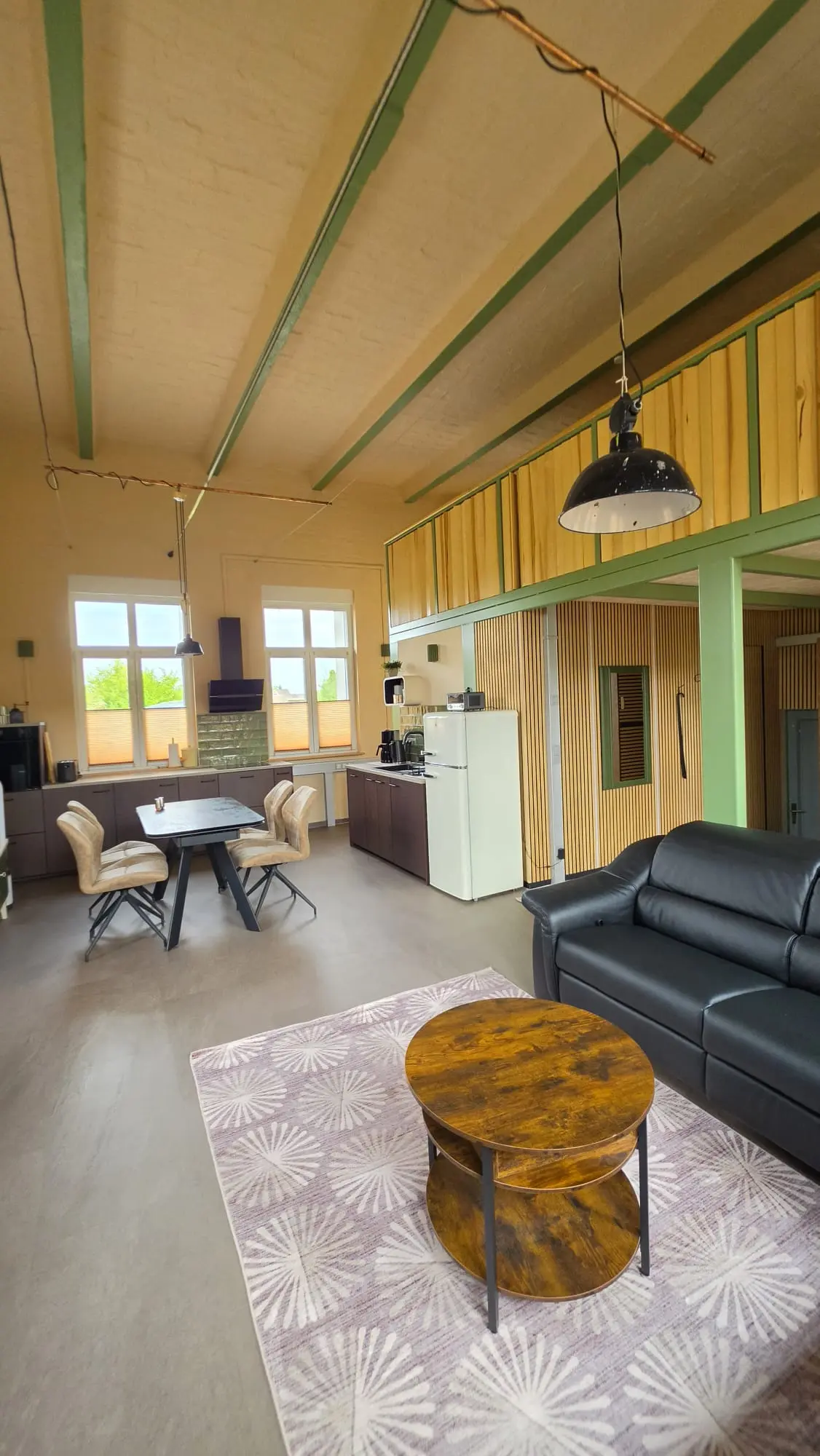 Offener Wohn- und Essbereich der Ferienwohnung Zahna-Loft — Esstisch und Küchenzeile vor der hölzernen Lamellenwand der Galerieebene