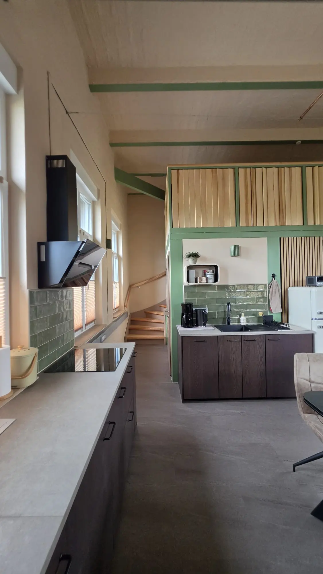 Offener Wohn- und Essbereich der Ferienwohnung Zahna-Loft — Küchenzeile mit grünen Fliesen, Wandregal und Kühlschrank neben der Treppe