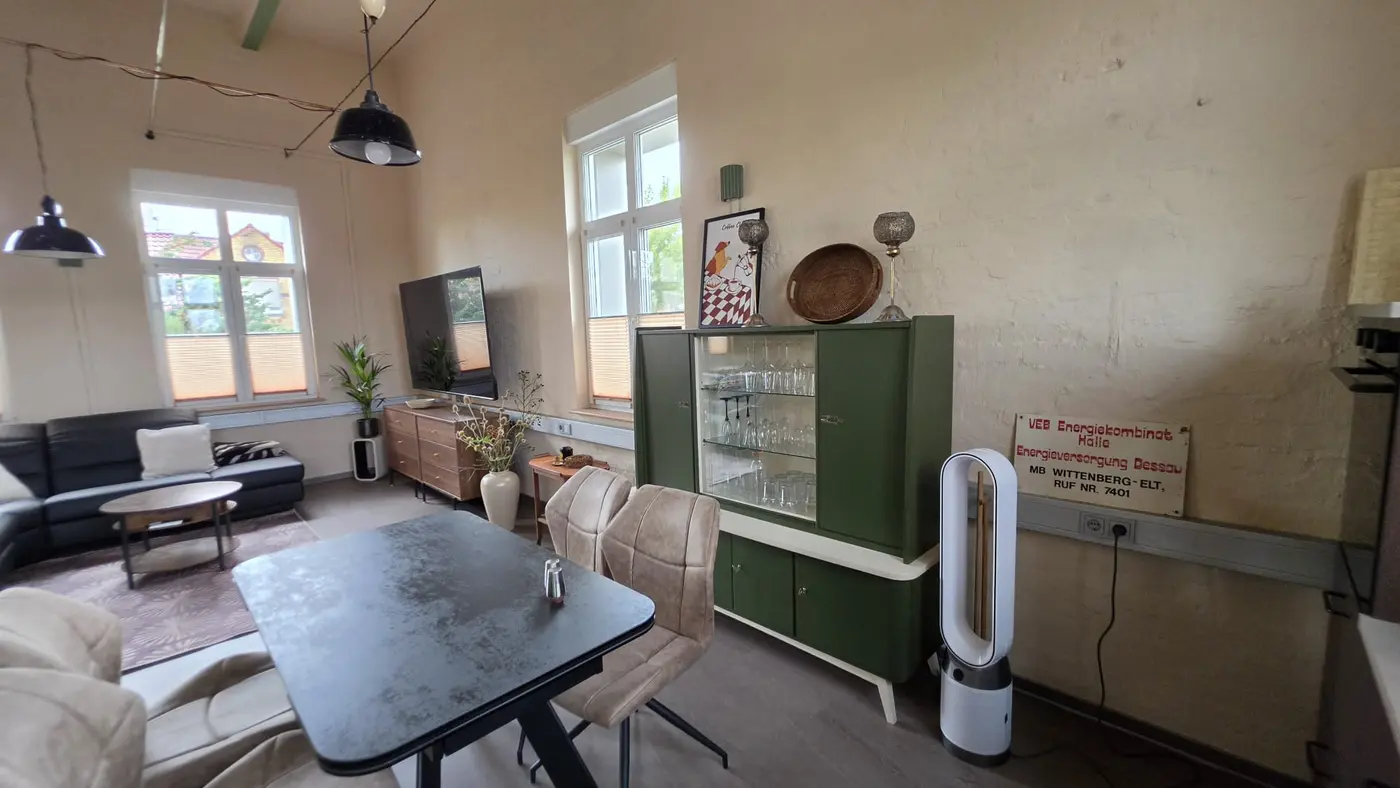 Offener Wohn- und Essbereich der Ferienwohnung Zahna-Loft — Esstisch neben der grünen Vintage-Vitrine mit Blick zum Sofa