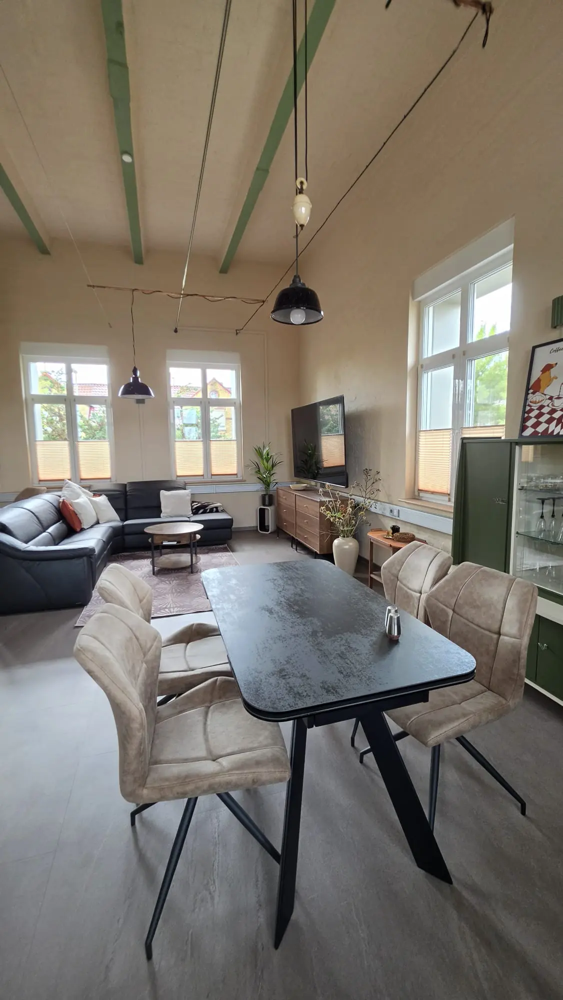 Wohn- und Essbereich mit Esstisch, schwarzer Ledercouch, Fernseher und grüner Vintage-Vitrine